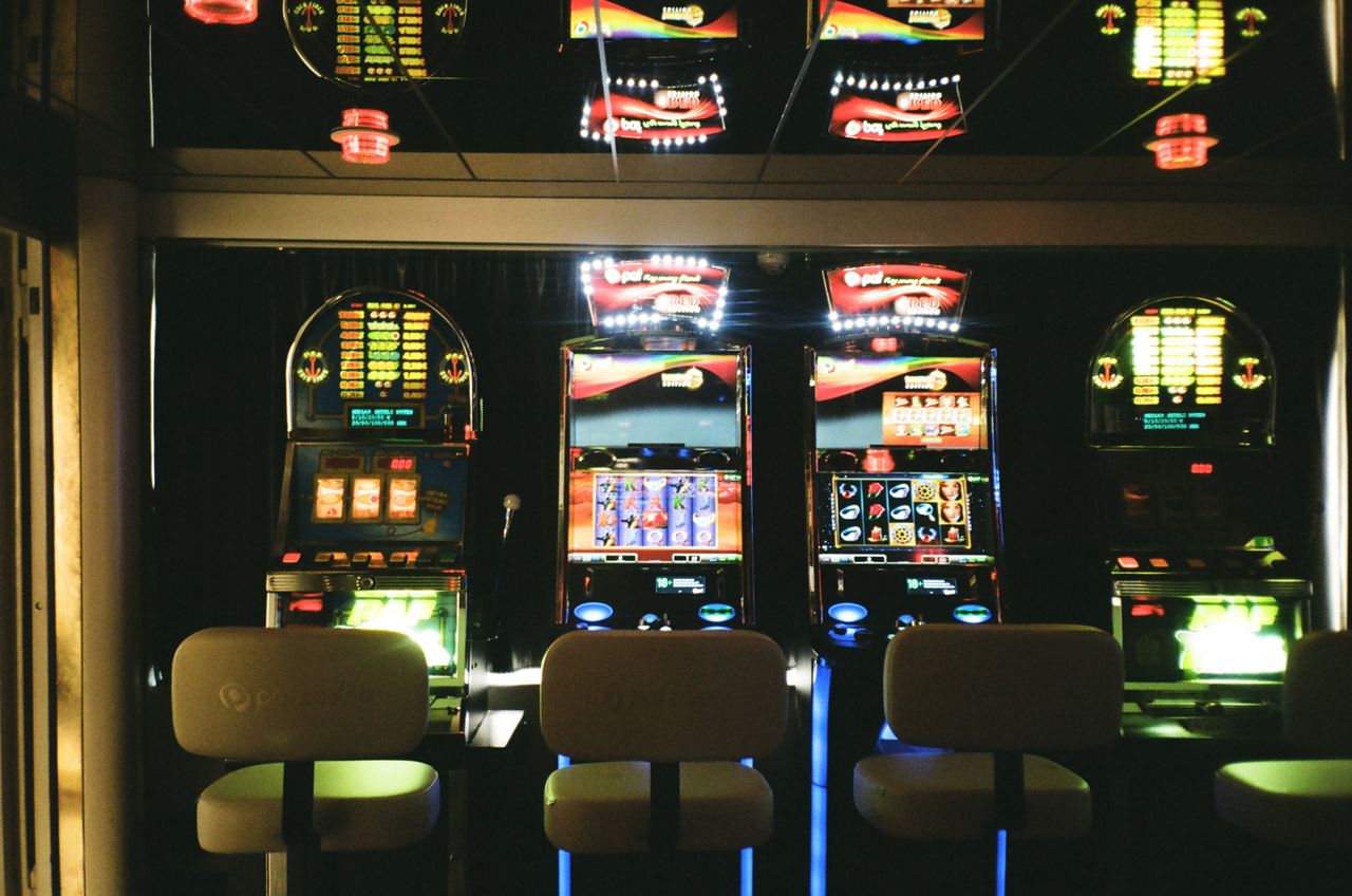 services-01 Slot machines in a dimly lit casino with reflective ceiling and empty chairs.
